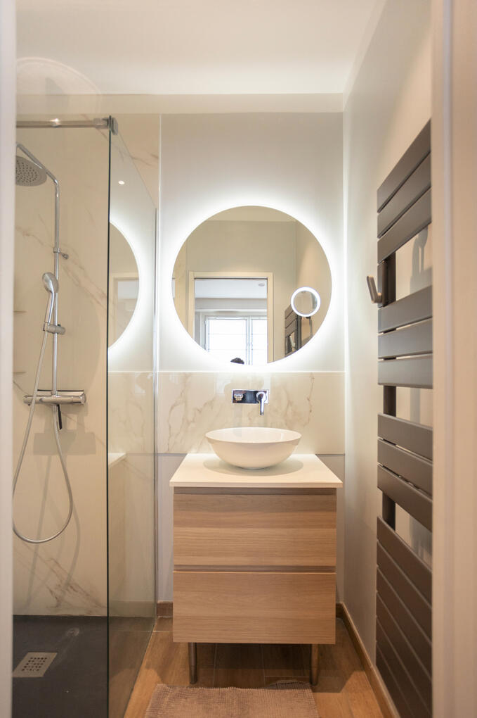 Salle de bain moderne, contemporaine avec son miroir LED circulaire et des matériaux chaleureux